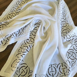 May include: A white table runner featuring a central smooth fabric panel flanked by wide borders of intricate cutwork lace. The lace pattern consists of repeating circular motifs with cross-shaped centers, creating a delicate openwork design.
