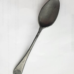 May include: A vintage silver spoon with a long handle and an oval bowl. The spoon has a slightly tarnished appearance, suggesting age. The handle's end features an embossed design with the text "1776 CLINTON COIN 1976".