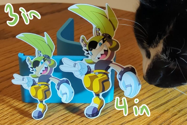 May include: Two cartoon character stickers, one 3 inches tall and the other 4 inches tall. Both characters are yellow and green with black eyes and a black eyepatch. They are wearing black and yellow outfits and have a white glove on each hand. The characters are on a blue background.