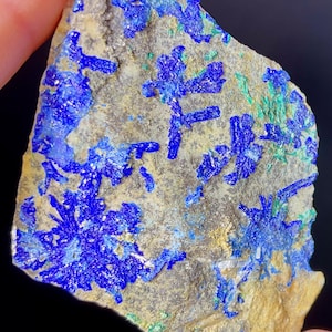 May include: A close-up of a rough, light brown rock with blue and green mineral deposits. The blue mineral is in the shape of small, delicate crystals.