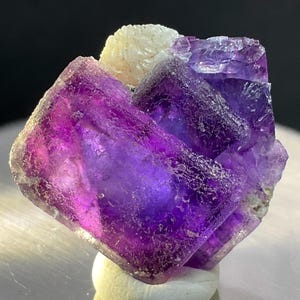 May include: A cluster of purple fluorite crystals with a white calcite crystal on top. The fluorite crystals are translucent and have a glassy luster.