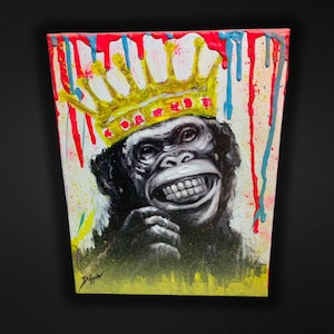 May include: A colorful painting of a smiling chimpanzee wearing a gold crown with red jewels. The artwork features a white background with red, blue, and yellow paint drips. The artist's signature is in the bottom left corner.