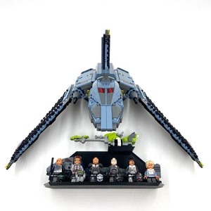 May include: A grey and black Lego spaceship with a green cockpit and a black stand. The spaceship has a long, thin body and two large wings. There are eight Lego minifigures standing on the stand.