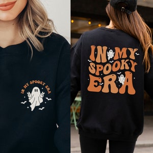 May include: Black sweatshirt with the text "IN MY SPOOKY ERA" in orange and white, featuring a ghost and bats. The front of the sweatshirt has a smaller version of the design. Perfect for Halloween.