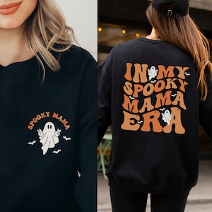 May include: Black sweatshirt with the text "Spooky Mama" and a ghost graphic on the front. The back of the sweatshirt features the phrase "In My Spooky Mama Era" with ghost and bat graphics in orange and white.