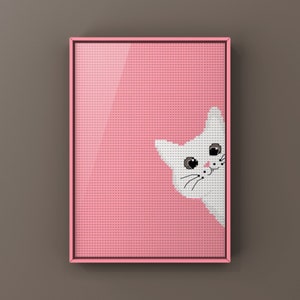 May include: A pink framed cross-stitch with a white cat peeking out from the right side of the frame. The cat has black eyes and a black nose.