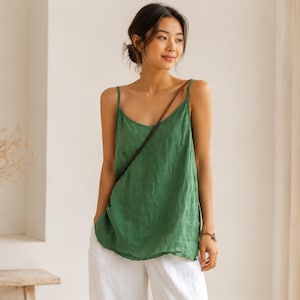 Peut inclure: Un haut caraco vert sans manches avec de fines bretelles et une encolure dégagée, associé à un pantalon blanc ample. Le haut présente une coupe décontractée et fluide avec un aspect texturé, porté avec une fine bandoulière marron.