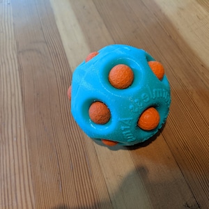 May include: A teal blue dog toy with orange rubber nubs. The toy is shaped like a ball and has the words "Zuru" and "smile" printed on it.