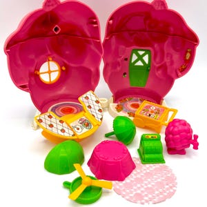 Puede incluir: Un juego de plástico rosa vintage, abierto para revelar detalles interiores. Incluye un columpio amarillo y blanco, accesorios verdes y rosas y una regadera amarilla. El juego está diseñado para parecerse a una fresa.