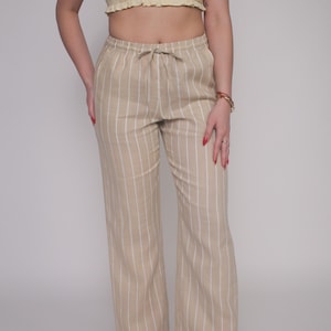 May include: Tan and white striped pants with a matching yellow crop top. The pants have a drawstring waist and a wide leg. The outfit is paired with black pointed-toe heels.