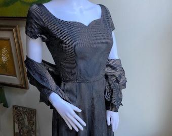 May include: A black and white polka dot dress with a sweetheart neckline and short sleeves. The dress has a full skirt and is made of a lightweight fabric. It is paired with a matching black and white polka dot shawl.