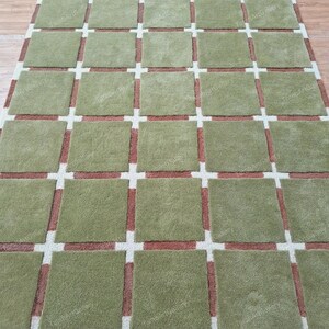 May include: A green and brown patterned rug with a grid design. The rug has a soft, plush texture.
