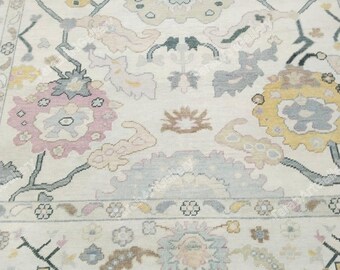 May include: A cream-colored rug with a floral pattern in shades of pink, yellow, and gray. The rug has a fringe border.