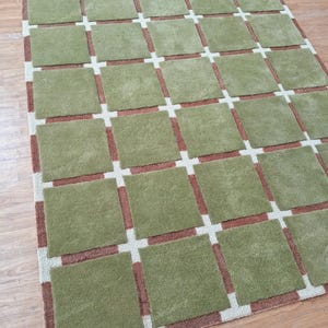 May include: A green and brown area rug with a geometric pattern. The rug has a grid pattern with squares of green and brown.