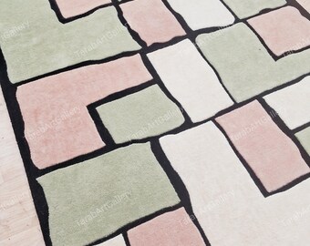 May include: A geometric rug with a black outline and pink, green, and white squares. The rug has a modern design and is made of soft, plush material.