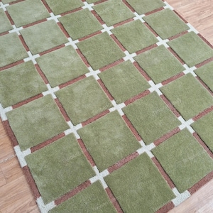May include: A green and brown area rug with a geometric pattern of squares. The rug has a light brown border.