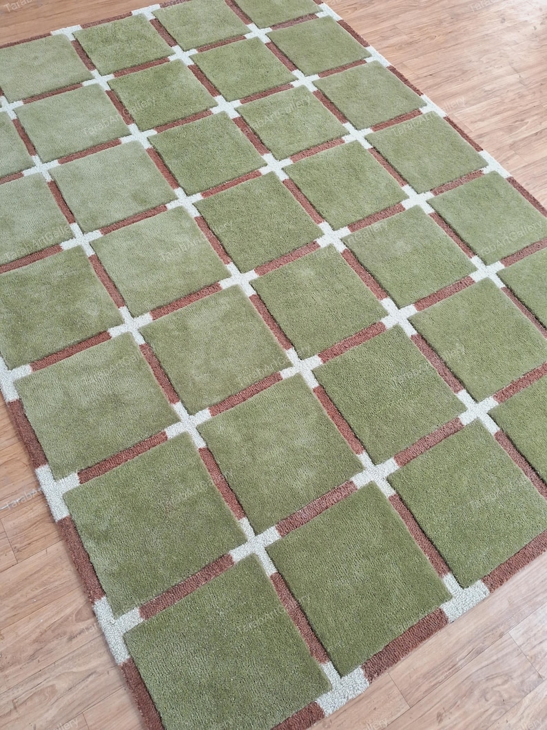 May include: A green and brown area rug with a geometric pattern of squares. The rug has a light brown border.