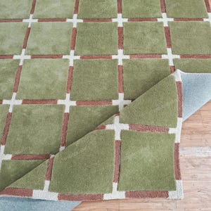 May include: A green and brown patterned rug with a checkered design. The rug is folded in half and the underside is visible.