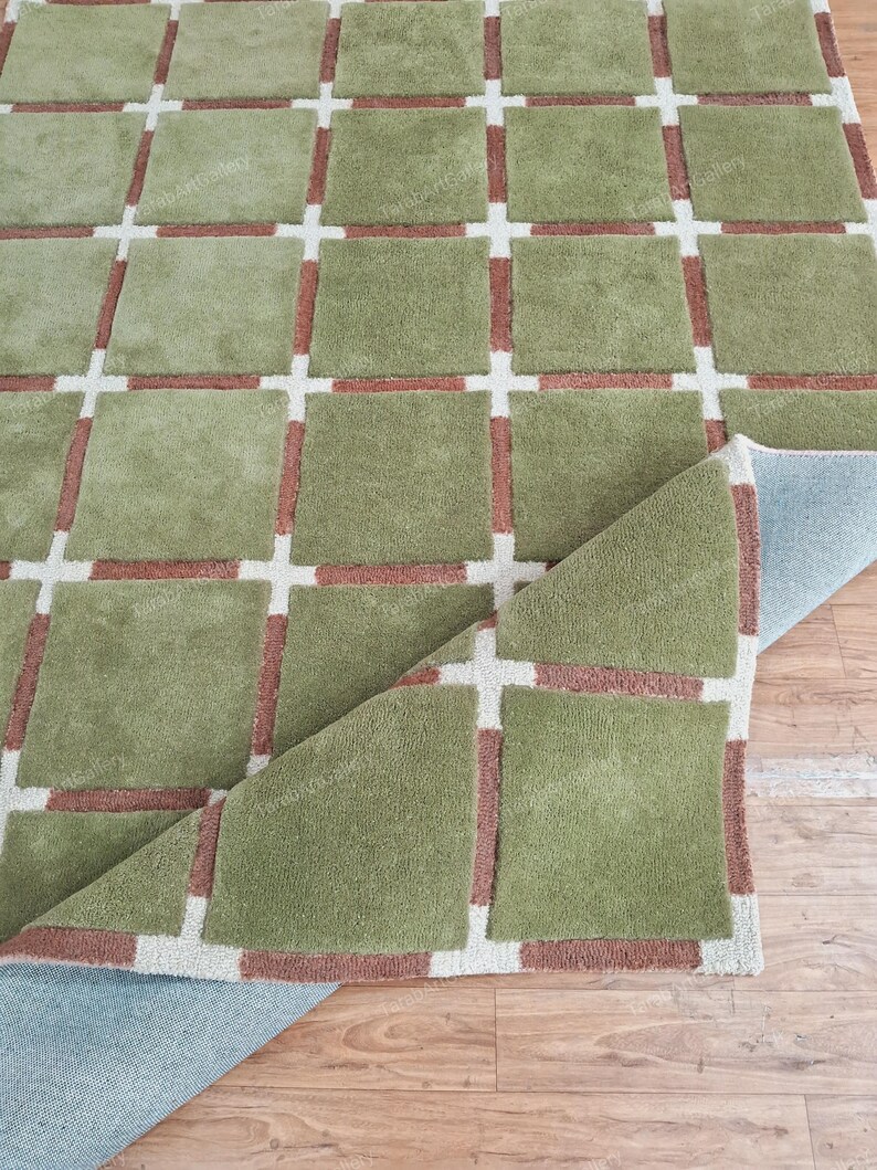May include: A green and brown patterned rug with a checkered design. The rug is folded in half and the underside is visible.