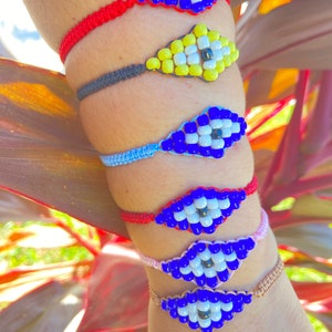 May include: Five colorful beaded bracelets with an evil eye charm. The bracelets are red, black, blue, red, and pink. The evil eye charms are blue, yellow, blue, blue, and blue.