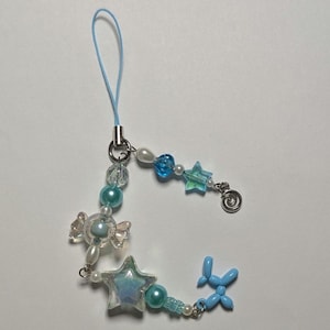May include: A blue and white beaded phone charm with a candy, star, and balloon charm. The charm is attached to a blue string.