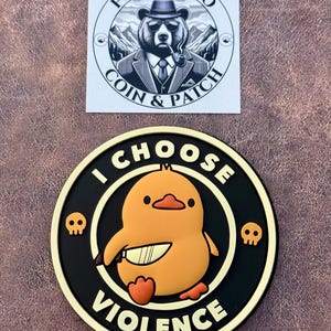 May include: Two patches and a sticker. The sticker features a bear in a suit with a pipe. The round patch has a cartoon duck holding a knife with the text "I CHOOSE VIOLENCE".