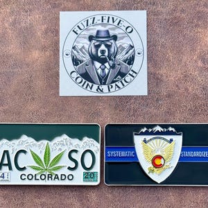 May include: Three metal patches and a sticker. The sticker features a bear in a suit with a pipe. One patch is a Colorado license plate design with a cannabis leaf. The other patch has a shield design with the text "Systematic Standardized".