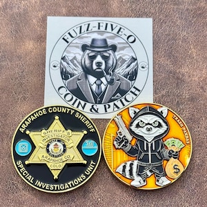 May include: A collection of collectible coins and a patch. One coin features a raccoon in a hoodie holding a gun and money, labeled "Trash Pandas." Another coin is a Sheriff's Investigator badge. The patch has a bear wearing a suit and hat.