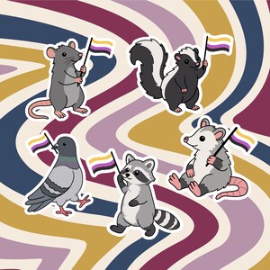 Peut inclure: Un ensemble de cinq autocollants de dessin animé représentant un rat gris, une mouffette noire et blanche, un pigeon gris, un raton laveur gris et un opossum blanc et gris, chacun tenant un petit drapeau non binaire jaune, blanc, violet et noir.