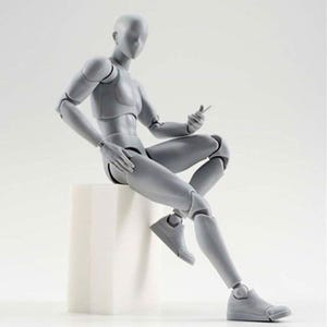 May include: A gray articulated figure sitting on a white cube. The figure is posed with one leg extended and the other bent at the knee. The figure has a neutral expression and is made of plastic.