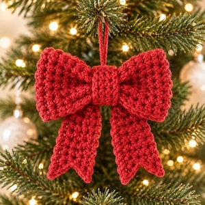 May include: A bright red crocheted bow ornament featuring a central knot and two long, dangling tails with pointed ends. The bow is constructed from yarn with a visible textured stitch pattern and includes a matching red loop for hanging.