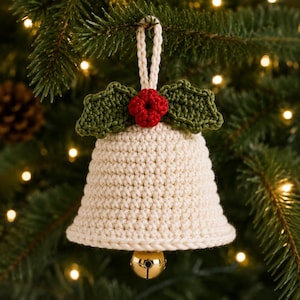 Può includere: Un ornamento a forma di campana lavorato all'uncinetto color crema, caratterizzato da due foglie di agrifoglio verde scuro e un piccolo grappolo di bacche rosse all'uncinetto sulla parte superiore. Un cappio intrecciato color crema.