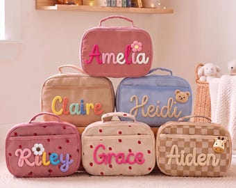 May include: Six rectangular corduroy storage bags with top handles and zippered closures. Each bag features a personalized name in colorful, textured yarn lettering and a small decorative applique, including flowers, a bear, and a giraffe.