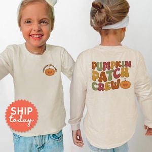 May include: Cream-colored long-sleeve shirt with a pumpkin graphic and the text "Pumpkin Patch Crew". The shirt is worn by a child. The graphic is in shades of orange, brown, and green.