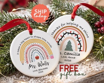 May include: Two round white ceramic ornaments with red ribbon hangers. One features a rainbow pencil design with the text 'it takes a big heart to shape little minds', 'Ms. Wells', 'LOVE, BENJAMIN', and '2026'. The other has a rainbow with lights, a tree, 'thanks for helping me shine', 'Ms. Camilla', 'Love, Anna', and '2026'.