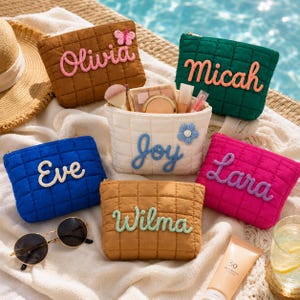 May include: Six quilted zippered pouches in brown, green, white, blue, pink, and tan, each featuring a personalized name in raised yarn lettering. The white pouch contains makeup brushes and cosmetics, accompanied by sunglasses and sunscreen.