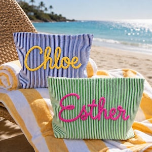 May include: Two zippered pouches with vertical stripes. One pouch is blue and white with the name Chloe in yellow rope lettering. The other pouch is green and white with the name Esther in pink rope lettering. Both pouches are rectangular.