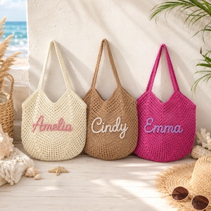 May include: Three crochet tote bags with open-knit patterns and two shoulder straps each. The cream bag features the name Amelia in pink, the tan bag features the name Cindy in white, and the magenta bag features the name Emma in purple.