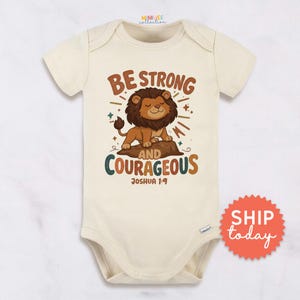 May include: Cream-colored baby bodysuit with a lion graphic and the text "BE STRONG AND COURAGEOUS" and "Joshua 1:9". The lion is brown and tan, sitting on a rock. The bodysuit has short sleeves and a snap closure.