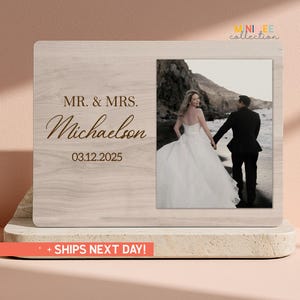 May include: A wooden photo frame with a light wood grain finish. The left side features the text "MR. & MRS. Michaelson" and the date "03.12.2025" in a script font. The right side holds a photograph of a couple in wedding attire.