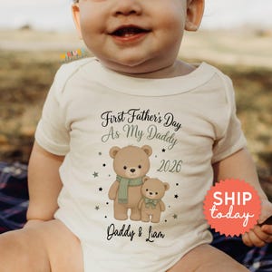 May include: A cream-colored baby onesie with the text "First Father's Day As My Daddy 2026" and the names "Daddy & Liam". The onesie features illustrations of two teddy bears wearing scarves and bow ties. The image includes a "SHIP today" sticker.