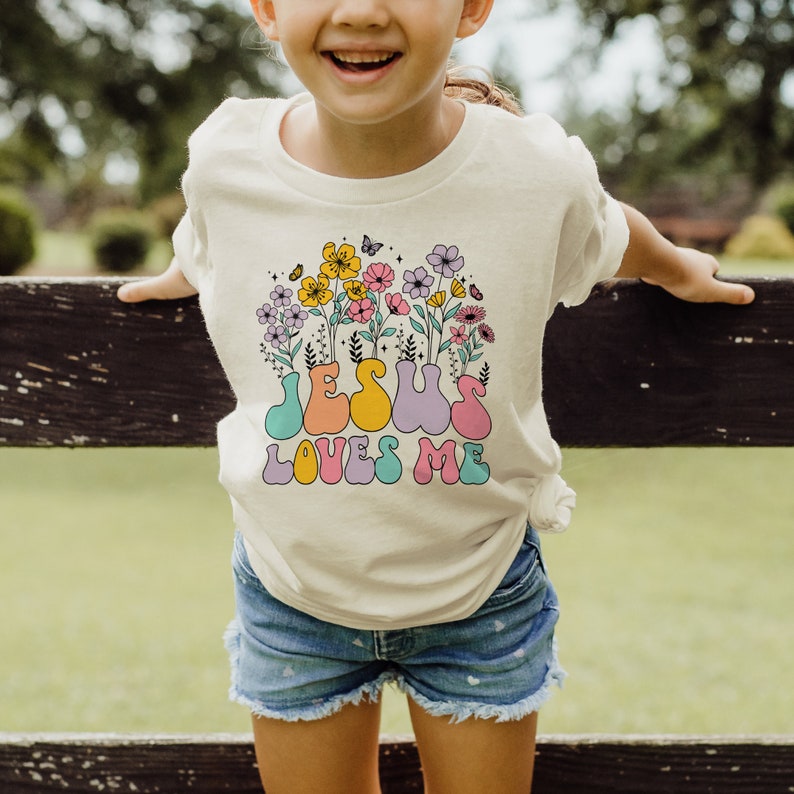 a little girl wearing a t - shirt that says jesus loves me