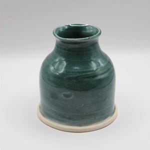 May include: A handcrafted, teal-colored ceramic vase with a wide base and a slightly flared top. The vase has a smooth, glossy finish and a light-colored rim. The vase is approximately 6 inches tall.
