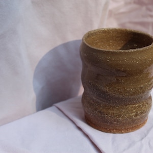 May include: A brown ceramic mug with a textured, uneven surface. The mug has a wide, rounded opening and a slightly flared base.