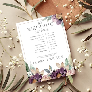May include: A white wedding ceremony details card with gold trim and a watercolor floral design featuring purple, pink, and green flowers. The card lists the wedding ceremony schedule with times for the processional, words of welcome, readings, vows, first kiss, unity ceremony, final blessings, and recessional. The card is signed "Olivia & Wilson".