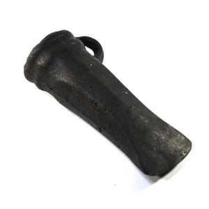 May include: A dark grey, weathered metal splitting wedge with a textured, pitted surface. The tool features a wide, rounded striking head at one end, a tapered body, and a sharp, flat edge at the opposite end for splitting wood or stone materials.