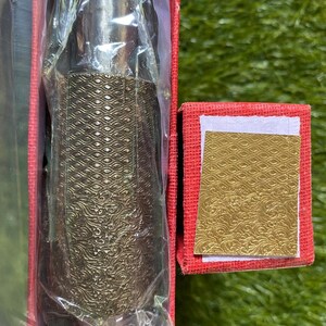 以下が含まれることがあります： 詳細なテクスチャデザインが施された、銀色の装飾ボトルストッパー。赤い箱に梱包されています。ストッパーは透明なプラスチックを通して部分的に見えます。お揃いの模様の小さな金色のカードが隣にあります。