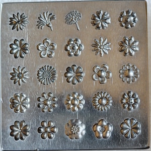 May include: A silver metal flower-shaped stamp plate with 20 different floral designs. The flowers vary in style, from simple to detailed, and are arranged in a grid pattern on the rectangular plate. The plate has a brushed metal finish.