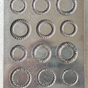 May include: A rectangular metal plate with multiple circular impressions. Each circle has a decorative border with various patterns. The plate's surface is a uniform, brushed metal finish, creating a consistent aesthetic.