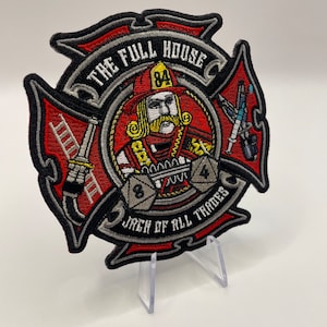 May include: An embroidered patch featuring a firefighter holding dice and a ladder. The patch is shaped like a cross and has the text "The Full House Jack of All Trades" around the edge.